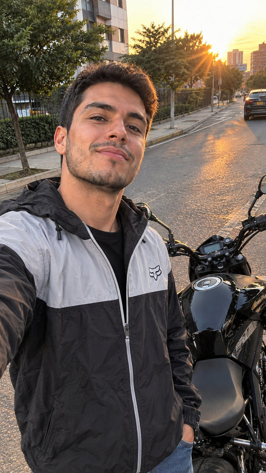 Selfie de motociclista con chaqueta cortavientos negra junto a su moto