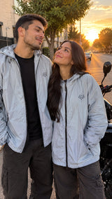 Pareja con chaquetas cortavientos unisex grises junto a su moto al atardecer