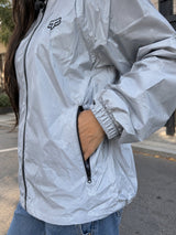 Detalle de chaqueta cortavientos gris: bolsillo con cierre y puño elástico