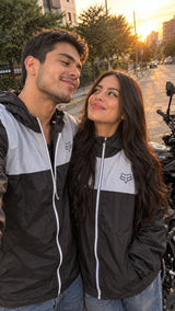 Pareja con chaquetas cortavientos unisex negras junto a su moto al atardecer